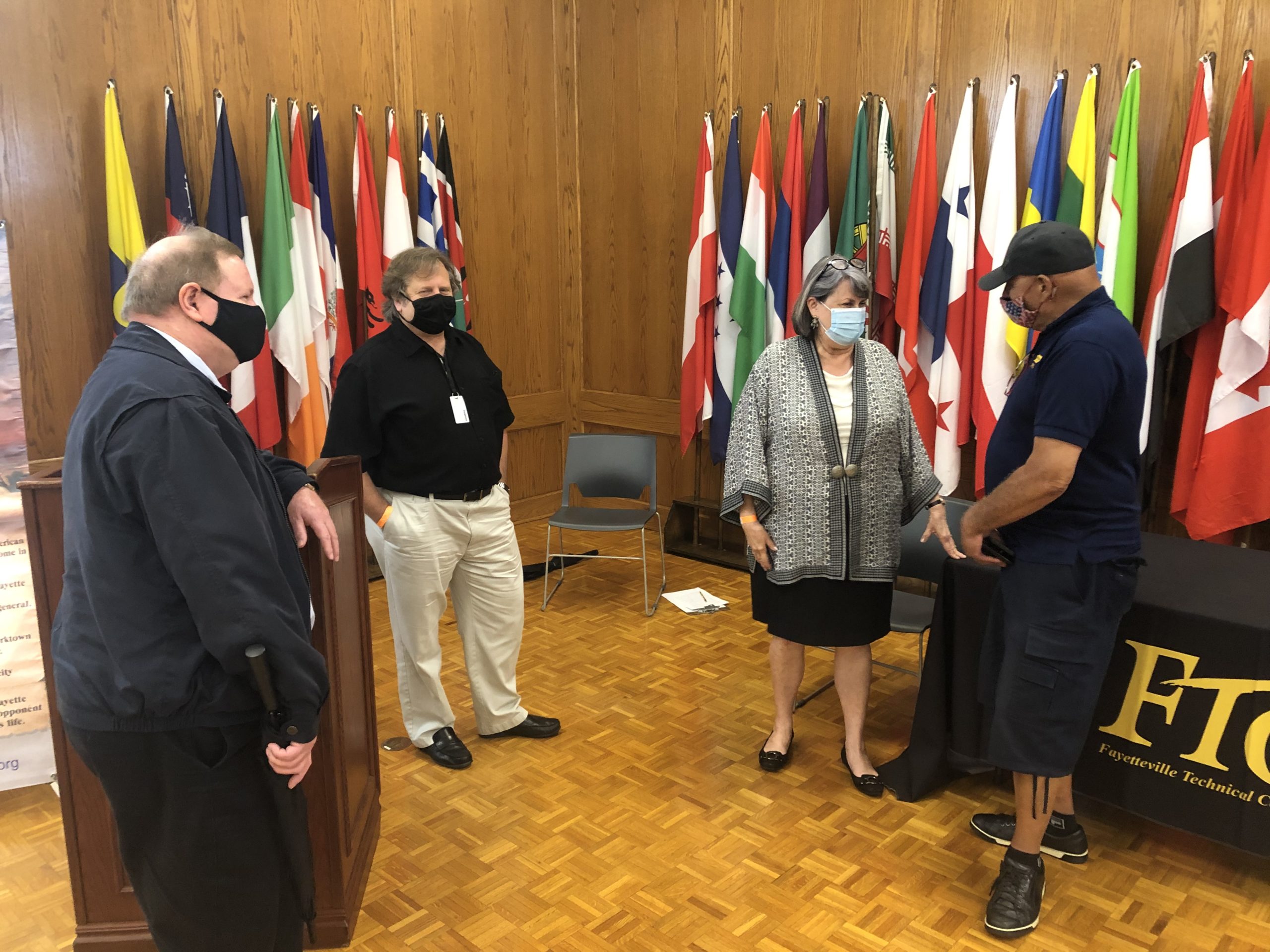 Three men and a woman in a university lecture room with flags in the background